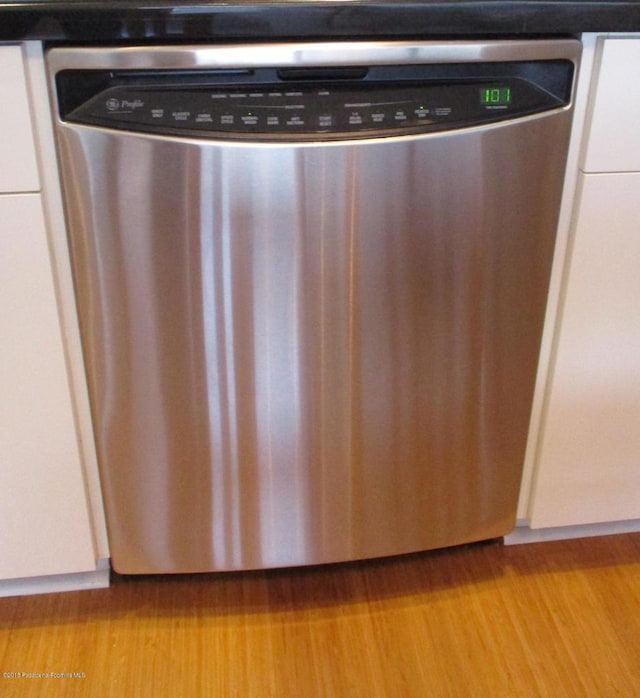 details with stainless steel dishwasher, white cabinets, and light wood-type flooring