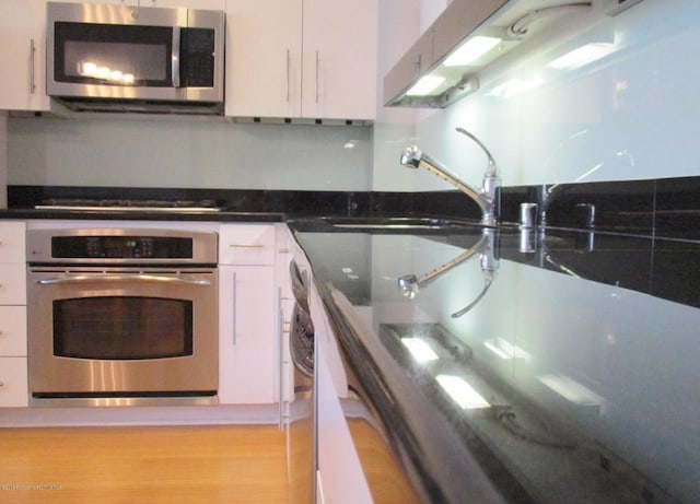 kitchen with stainless steel appliances, sink, light hardwood / wood-style flooring, and white cabinets