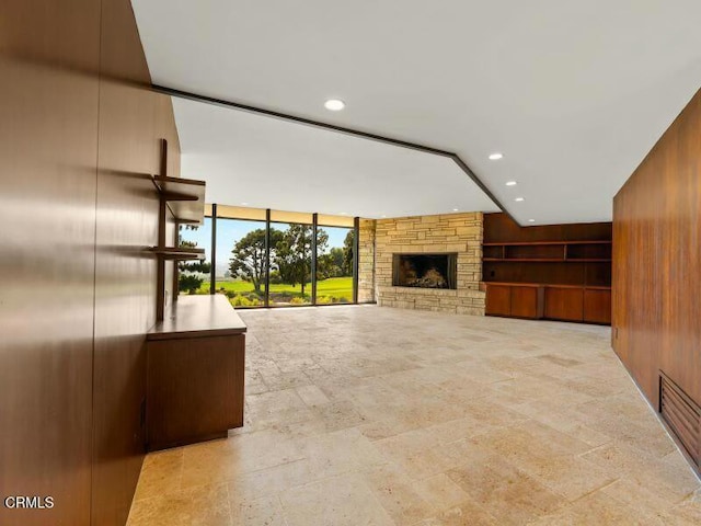 unfurnished living room featuring wooden walls and a stone fireplace