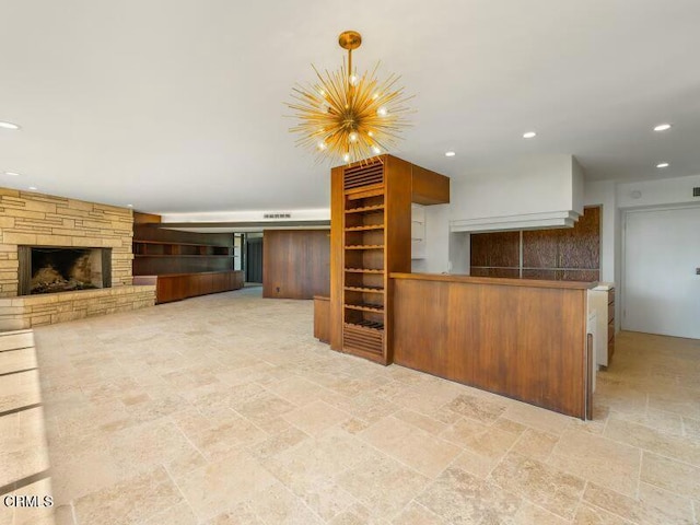 kitchen featuring open floor plan, a peninsula, stone finish flooring, a fireplace, and recessed lighting