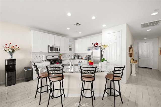 kitchen featuring sink, white cabinetry, a center island with sink, stainless steel appliances, and a kitchen bar