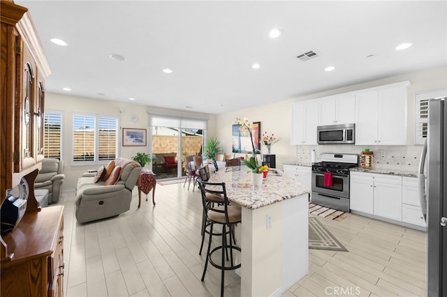 kitchen featuring appliances with stainless steel finishes, a center island, light stone countertops, and white cabinets