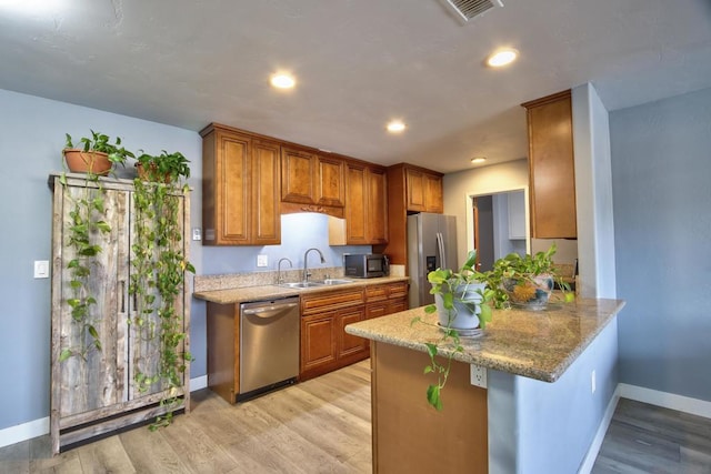 kitchen featuring sink, a breakfast bar, appliances with stainless steel finishes, light hardwood / wood-style floors, and kitchen peninsula