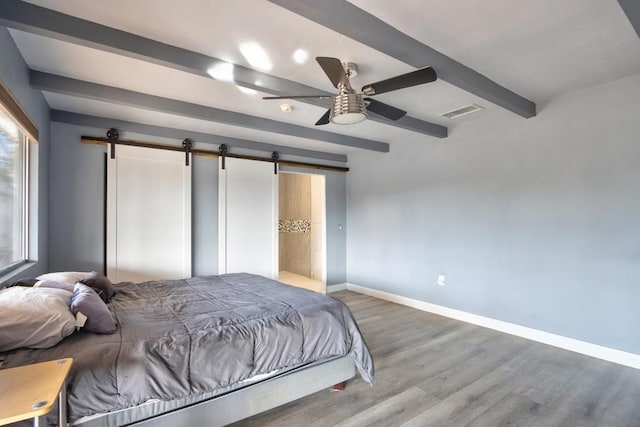 bedroom featuring beamed ceiling, a barn door, and hardwood / wood-style floors