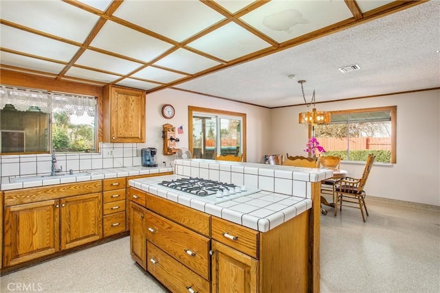 kitchen featuring sink, tile countertops, white gas cooktop, hanging light fixtures, and a textured ceiling