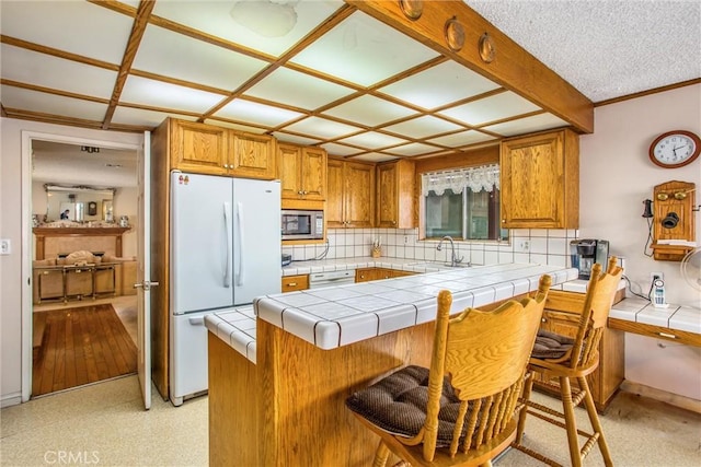 kitchen featuring tile countertops, stainless steel microwave, sink, a breakfast bar area, and white refrigerator