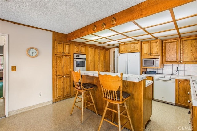 kitchen featuring a kitchen island, appliances with stainless steel finishes, a breakfast bar area, tile counters, and a textured ceiling