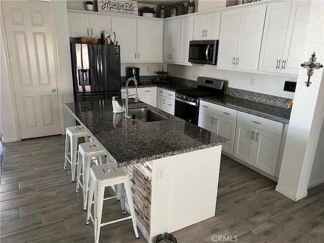 kitchen with sink, a breakfast bar, appliances with stainless steel finishes, white cabinetry, and a center island with sink