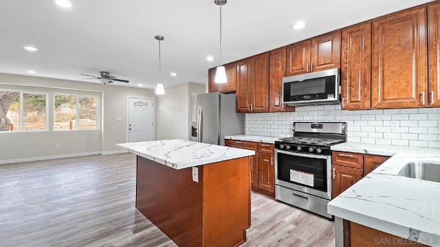 kitchen with pendant lighting, appliances with stainless steel finishes, light stone counters, and a kitchen island