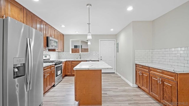 kitchen featuring hanging light fixtures, light wood-type flooring, a kitchen island, stainless steel appliances, and decorative backsplash