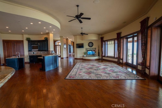 unfurnished living room with sink, dark wood-type flooring, ornamental molding, and ceiling fan