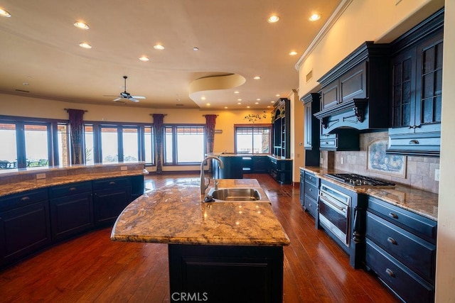 kitchen featuring sink, a kitchen island with sink, backsplash, stainless steel appliances, and dark hardwood / wood-style flooring