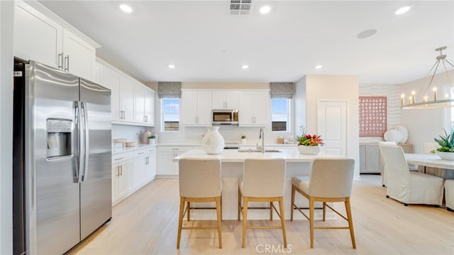 kitchen with an island with sink, a breakfast bar area, white cabinets, hanging light fixtures, and stainless steel appliances