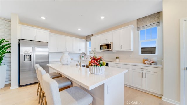 kitchen with appliances with stainless steel finishes, a kitchen island with sink, white cabinets, and a kitchen breakfast bar