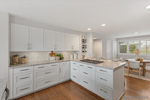 kitchen featuring white cabinetry, light stone counters, wood-type flooring, kitchen peninsula, and stainless steel gas stovetop