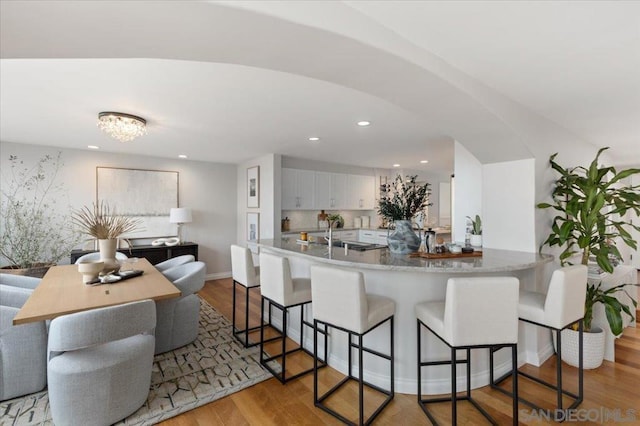 kitchen with a breakfast bar, sink, white cabinetry, light hardwood / wood-style flooring, and kitchen peninsula