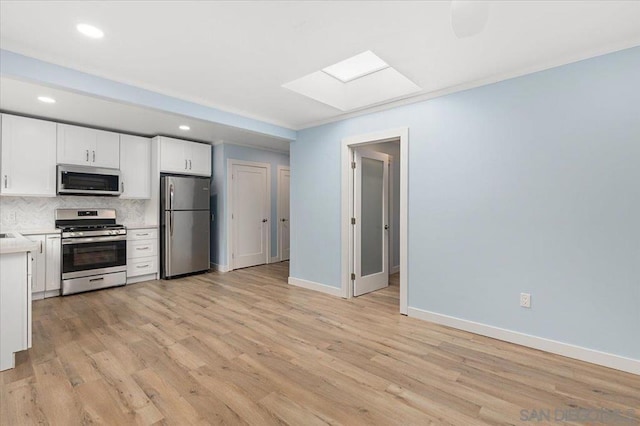 kitchen with appliances with stainless steel finishes, a skylight, white cabinets, backsplash, and light hardwood / wood-style floors