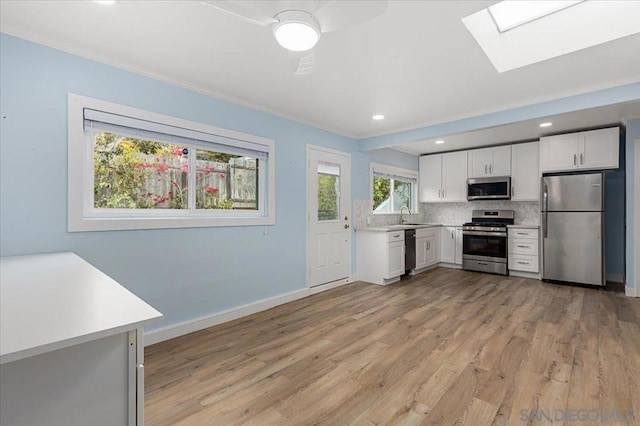 kitchen with a skylight, white cabinetry, sink, decorative backsplash, and stainless steel appliances