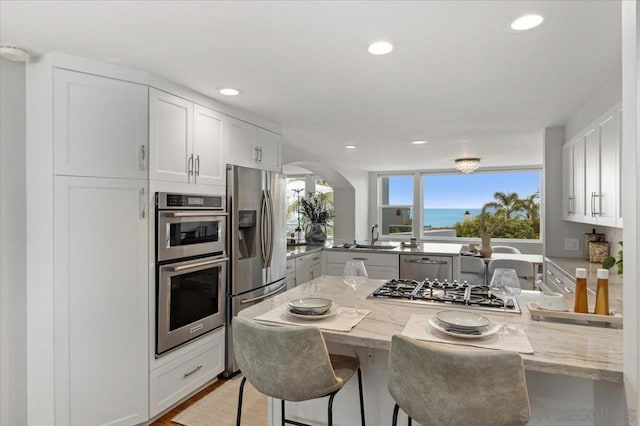 kitchen featuring white cabinetry, kitchen peninsula, light stone counters, and a breakfast bar area