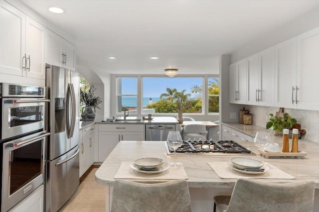 kitchen with appliances with stainless steel finishes, white cabinetry, sink, light stone counters, and a water view