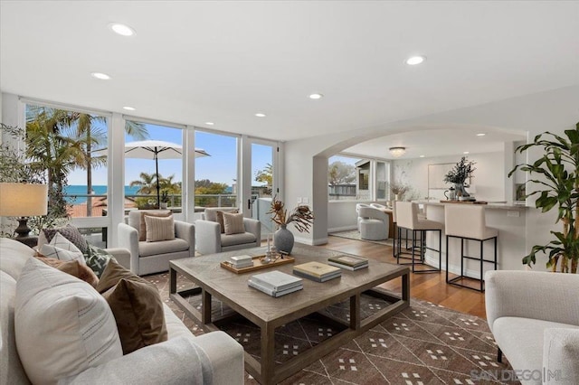 living room with dark hardwood / wood-style flooring, a water view, and a wall of windows