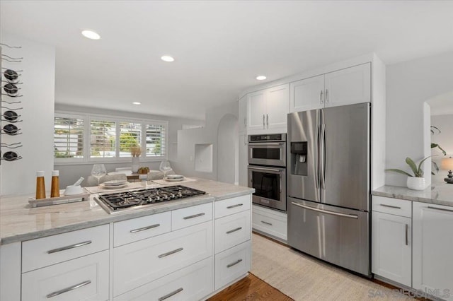 kitchen with white cabinetry, appliances with stainless steel finishes, light stone counters, and light wood-type flooring