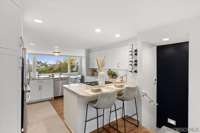 kitchen featuring sink, a breakfast bar, backsplash, stainless steel appliances, and white cabinets