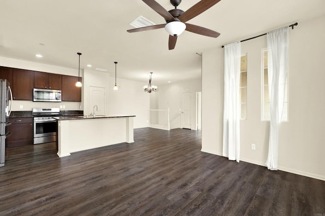 kitchen with appliances with stainless steel finishes, dark hardwood / wood-style floors, an island with sink, sink, and hanging light fixtures