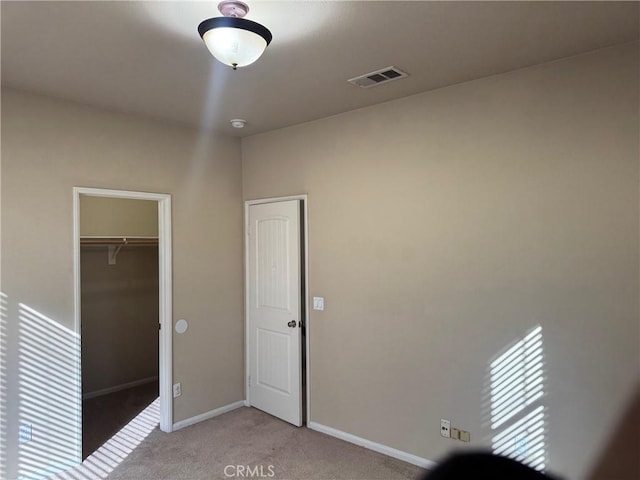 unfurnished bedroom featuring a walk in closet, light colored carpet, and a closet