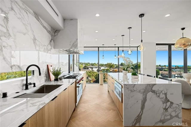 kitchen with a spacious island, sink, stainless steel appliances, light stone countertops, and wall chimney range hood