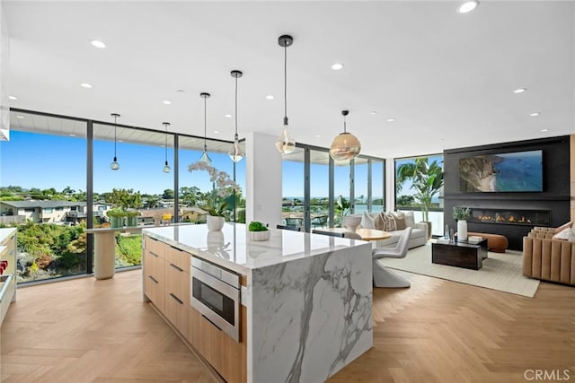 kitchen featuring a spacious island, hanging light fixtures, stainless steel microwave, light stone countertops, and light parquet floors