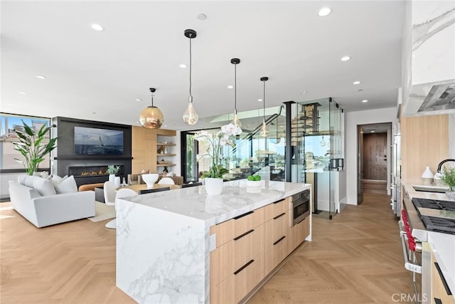 kitchen with sink, light parquet floors, a center island, light stone countertops, and decorative light fixtures