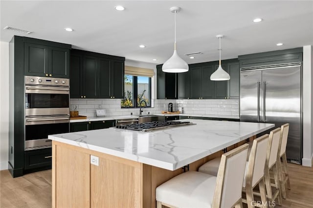 kitchen with decorative light fixtures, light wood-type flooring, stainless steel appliances, a large island, and light stone countertops