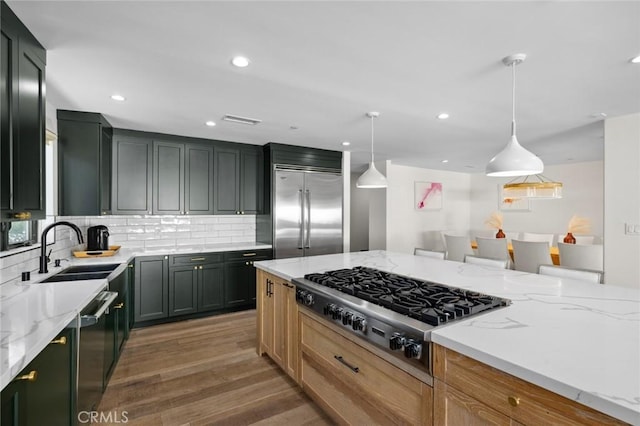 kitchen with light stone counters, hanging light fixtures, stainless steel appliances, and sink