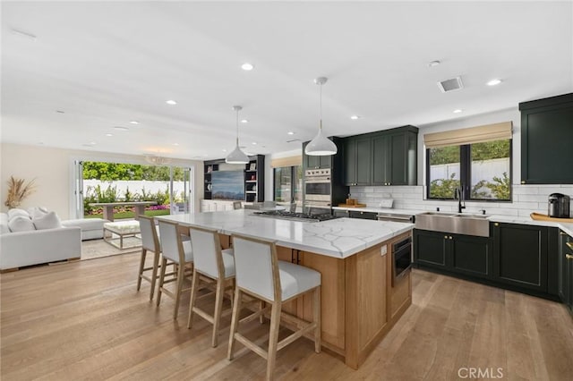 kitchen with pendant lighting, stainless steel gas stovetop, sink, a center island, and light stone countertops