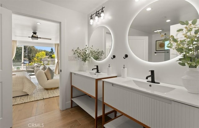 full bath with two vanities, ensuite bath, a ceiling fan, wood finished floors, and a sink