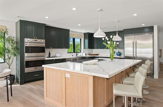 kitchen with light stone counters, a kitchen island, decorative backsplash, light wood finished floors, and appliances with stainless steel finishes