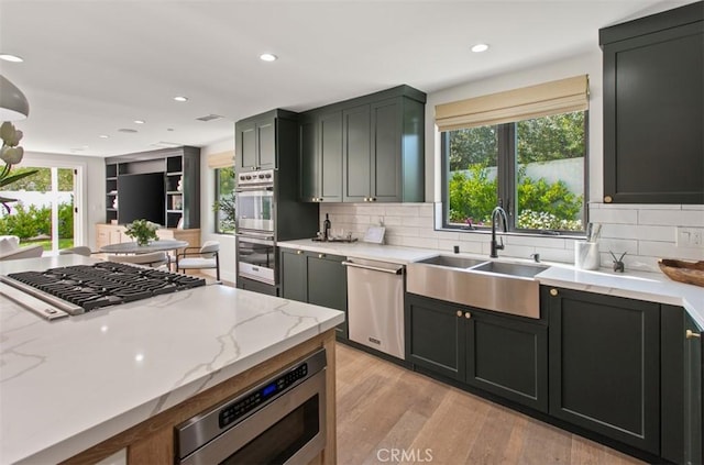 kitchen featuring tasteful backsplash, light wood-type flooring, light stone counters, appliances with stainless steel finishes, and a sink