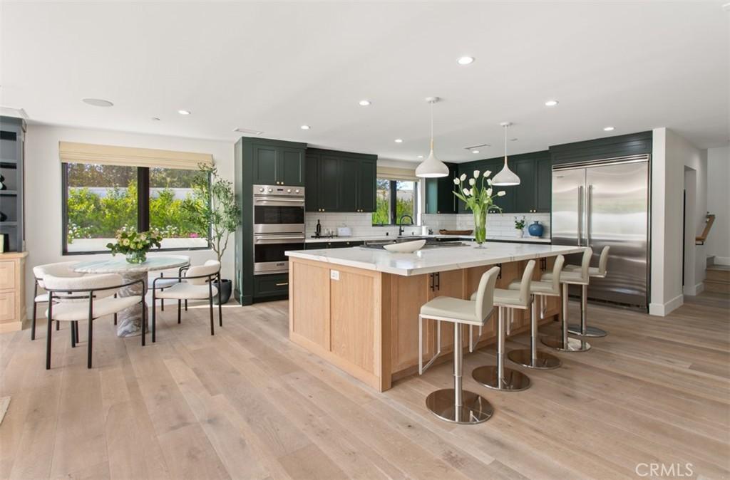 2626 Basswood St, Newport Beach, CA 92660 - kitchen featuring light wood-type flooring, a large island, appliances with stainless steel finishes, light countertops, and backsplash