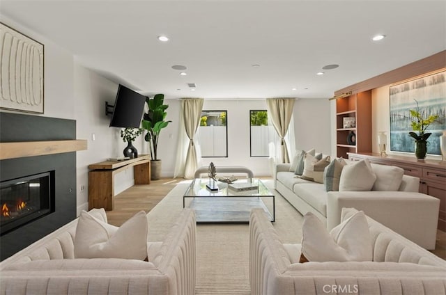 living room with a glass covered fireplace, recessed lighting, and light wood finished floors