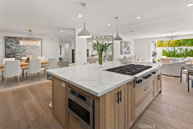 kitchen with light wood-type flooring, light stone counters, open floor plan, a kitchen island, and stainless steel appliances