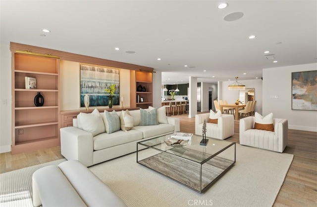 living room featuring built in shelves, recessed lighting, wood finished floors, and baseboards