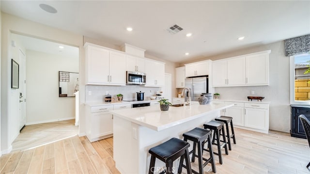 kitchen featuring white cabinetry, appliances with stainless steel finishes, a kitchen breakfast bar, and an island with sink