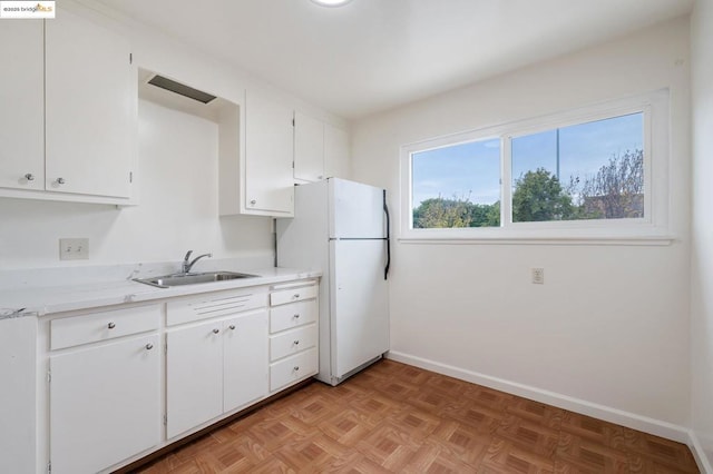 kitchen with white cabinetry, sink, light parquet floors, and white refrigerator