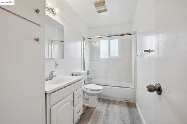 full bathroom with vanity, hardwood / wood-style flooring, shower / bath combination with glass door, and toilet