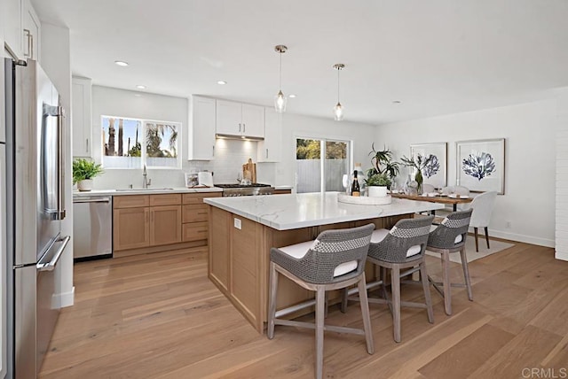 kitchen featuring appliances with stainless steel finishes, decorative light fixtures, a center island, light stone countertops, and white cabinetry