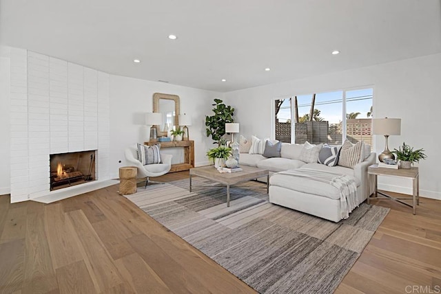 living room with a large fireplace, baseboards, light wood-style flooring, and recessed lighting