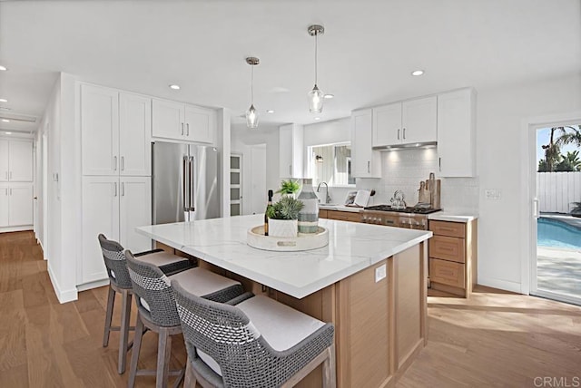 kitchen featuring light stone counters, stainless steel appliances, white cabinets, a center island, and decorative light fixtures