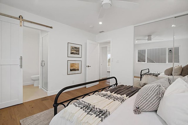 bedroom with a barn door, light wood-style flooring, recessed lighting, visible vents, and ensuite bath