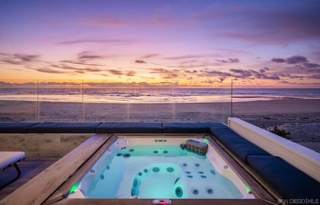 pool at dusk with an outdoor hot tub, a beach view, and a water view